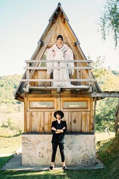 Bride stands on the balcony of a triangular house, above the groom standing on the pavement. High quality photo