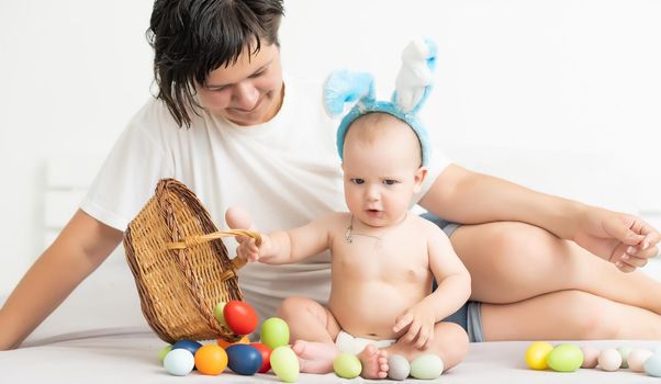 happy family celebrating easter mother and baby bunny ears at home with colorful eggs.