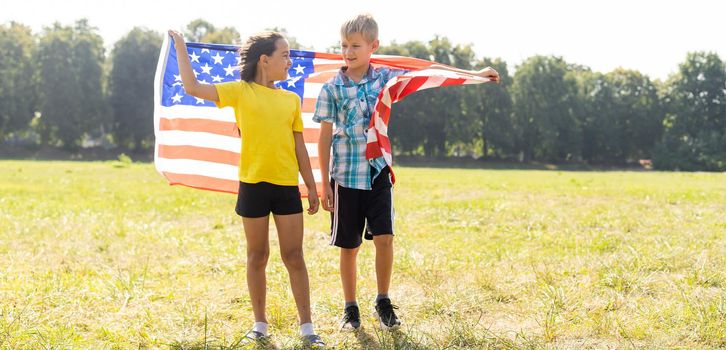 Happy Caucasian girl and boy smiling laughing holding hands and waving American flag outside celebrating 4th july, Independence Day, Flag Day concept