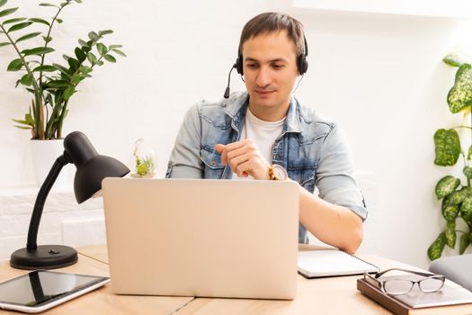 Focused young businessman in eyewear wearing headphones, holding video call with clients on laptop. Concentrated millennial man in glasses giving online educational class lecture, consulting customer.