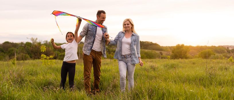 Happy family father, mother and child daughter launch a kite on nature at sunset.