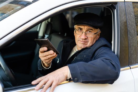 serious businessman driving his car and looking at smartphone.