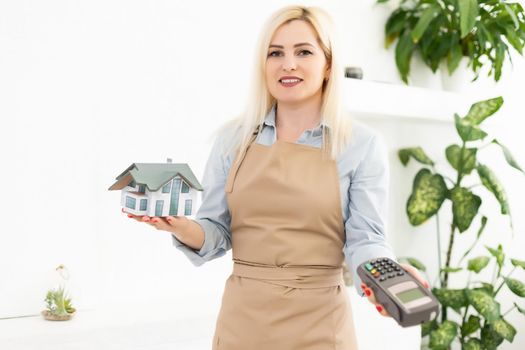 happy young woman holding a house layout and pos terminal