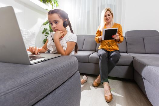 smiling young mother and daughter studying online classes in home office in the modern living room