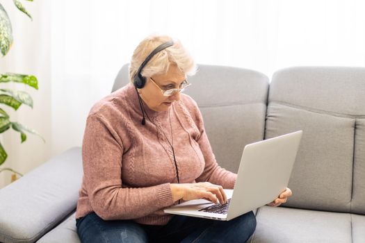 Elderly woman making video call on laptop, waving at screen, chatting with children, free space.