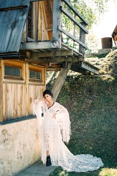 Woman in a white dress stands with her elbow resting on a wall of the house. High quality photo