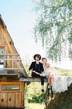 Bride and groom sit on a bridge near a house. High quality photo