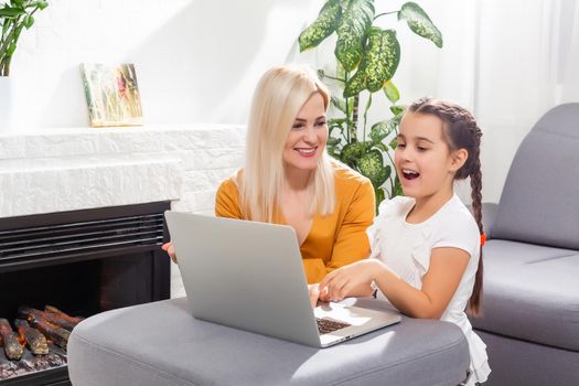 Smiling mother and toddler daughter looking at the notebook indoor. Distance online learning concept. Activities for kids during quarantine.