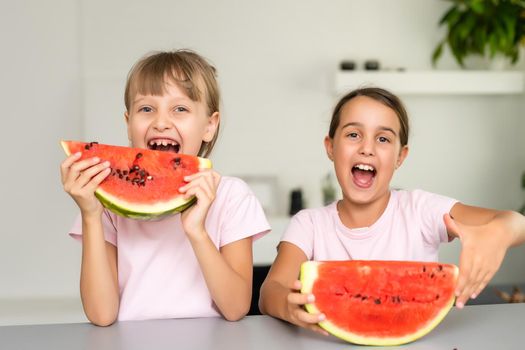 Funny little sisters eating fresh juicy watermelon at home.