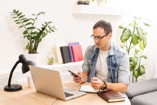 Smiling young man working on laptop in modern kitchen, checking email in morning, writing message in social network, happy young male using internet banking service, searching information