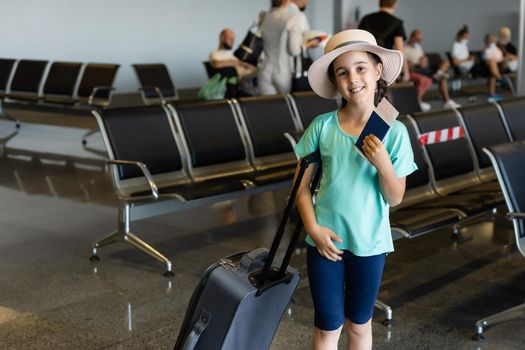 tourism, vacation, childhood and transportation concept - smiling little girl with travel bag, ticket and passport over airport background