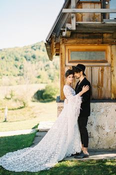 Groom hugs bride near the wall of a house. Side view. High quality photo
