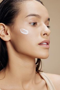 brunette applying a soothing face mask cosmetic beige background. High quality photo