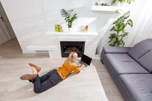 Happy smiling woman using laptop at living room at home, watching funny video, learning language, video calling, mother working online