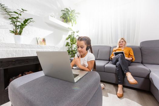 smiling young mother and daughter studying online classes in home office in the modern living room