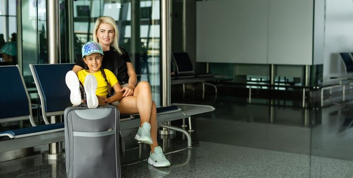 Mother with daughter in masks waiting for their flight at airport. Woman with little girl in international airport