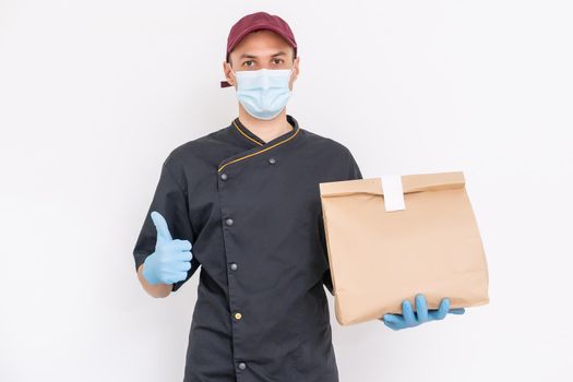 Delivery guy with protective mask and gloves holding box, bag with groceries in front of a building