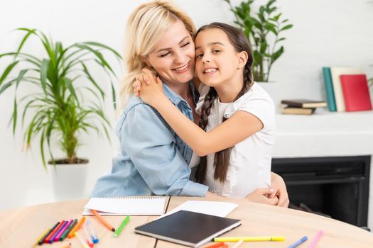 Beautiful school girl doing homework with mother at home.