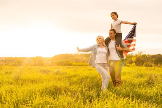 Patriotic holiday. Happy family, parents and daughters children girl with American flag outdoors. USA celebrate 4th of July