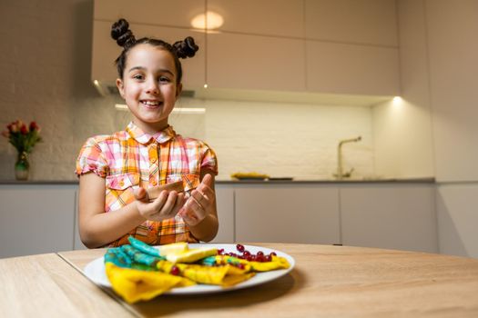 Mother preparing pancakes and daughter doing homework in the kitchen at home