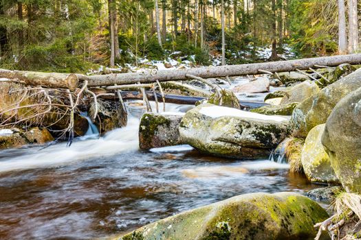 Huge stones and fallen trees lying over small mountain stream