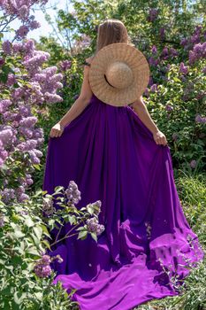 Fashion Model in Lilac Flowers, Young Woman in Beautiful Long Dress Waving on Wind, Outdoor Beauty Portrait in Blooming Garden.