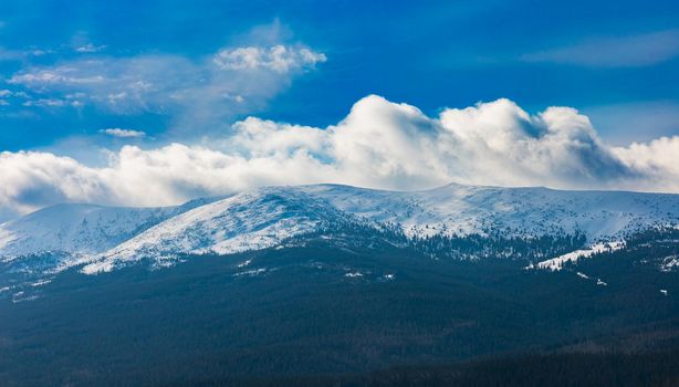 Foggy cloudy landscape seen from long distance of mountain ranges full of snow and giant clouds over it