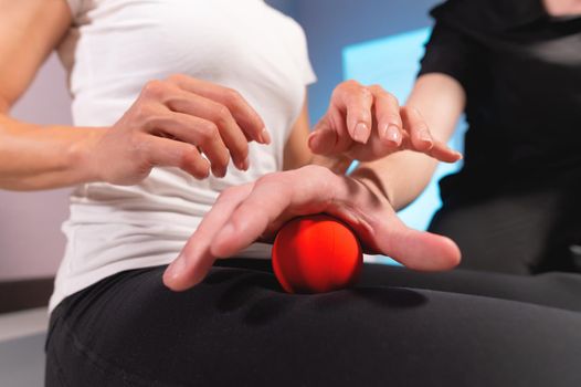 Close-up of a male massage therapist showing a client how to use and massage a ball. Myofascial thigh massage.