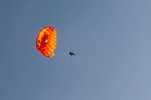 Parachute with flying man against blue sky background. Extreme vacation by the sea