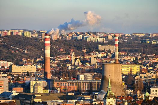 Steaming chimneys with houses in the city. Concept for environment and industry. Background with city landscape at sunset. Brno - Czech Republic - Europe.