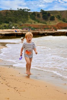 A little boy runs along the sandy beach along the seashore. Child resting on the sea