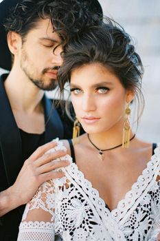 Groom in a hat hugs the bride in a white wicker dress. High quality photo