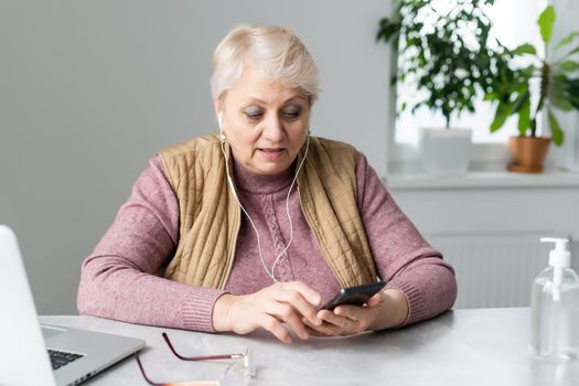 Elderly woman sitting at table typing on a smartphone.