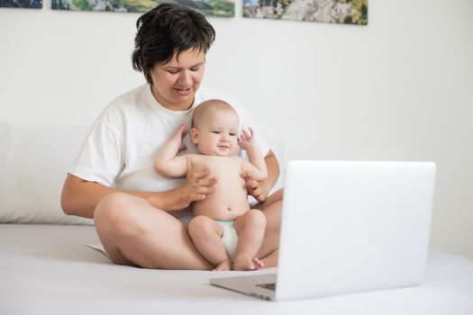 Woman with baby and laptop in bed