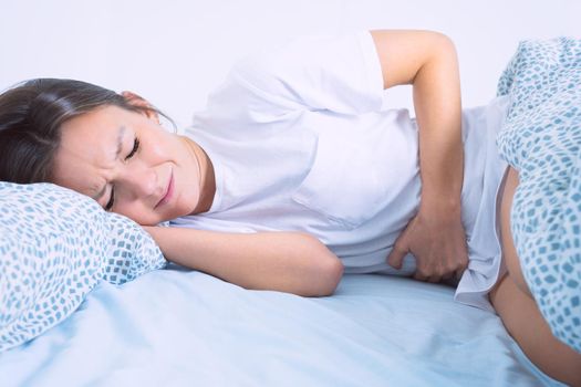 Woman in bed suffering from menstruation pain, stomach ache or abdominal pain. Menstruation period or PMS. High quality photo