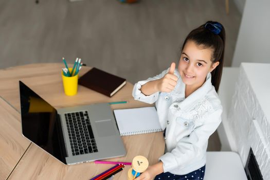 little girl with a laptop at the table and holds an hourglass, waiting for the end of online lessons