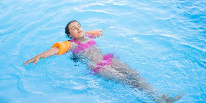 Pretty little girl swimming in outdoor pool and have a fun.