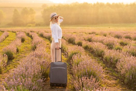 woman with suitcase in her hand in a lavender field in the summer afternoon.