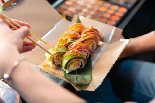 close up of chopsticks taking portion of sushi roll on the table restaurant. eating sushi roll using chopsticks.