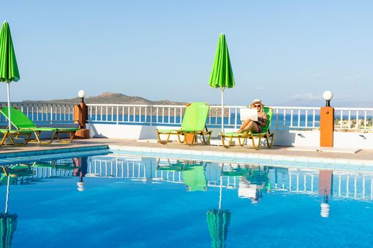 Woman using laptop computer by the swimming pool.