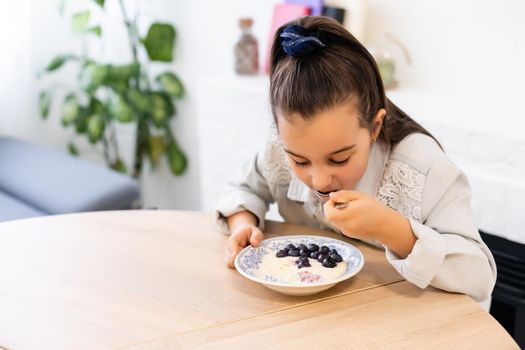 little girl eating porridge with blueberries at the table at home in the kitchen
