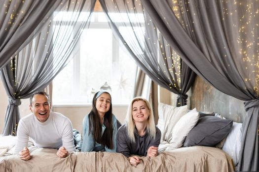 Smiling family lie on a white bed.