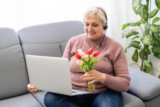 Cropped shot of a beautiful elderly woman using laptop computer while sitting with flowers.