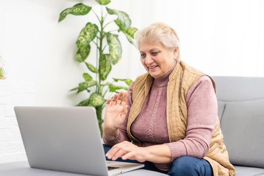 Serious mature older adult woman watching training webinar on laptop working from home or in office. 60s middle aged businesswoman taking notes while using computer technology.