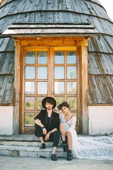 Bride and groom sit on the threshold of a wooden house. High quality photo
