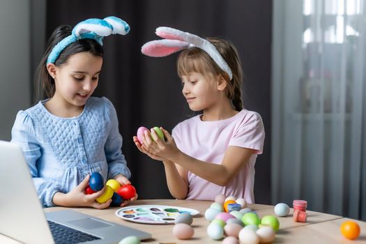 Two little cute girls with bunny ears are painting Easter eggs, children are preparing for the spring holiday, Easter mood, children are drawing on eggs