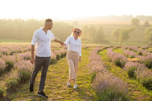 Smiling young couple embracing at the lavender field, holding hands, walking