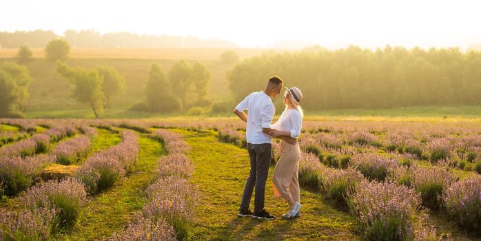 Smiling young couple embracing at the lavender field, holding hands, walking