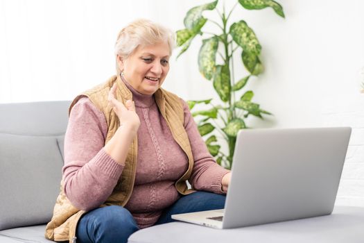 Elderly woman making video call on laptop, waving at screen, chatting with children, free space.