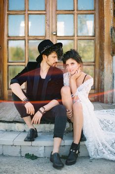 Groom turned his head to bride sitting on the threshold of a wooden house. High quality photo